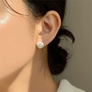 Close-up of a sterling silver smiley face stud earring worn on a model's ear