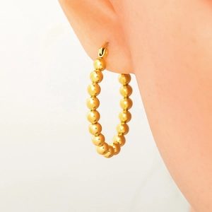 Detail of model wearing gold beaded hoop earrings in polished stainless steel finish