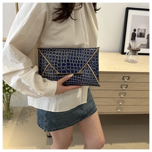 Navy blue envelope clutch bag with gold grid texture held in a hand for casual style
