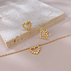 Gros plan détaillé de boucles d'oreilles et bracelet cœur dorés sur pierre et fond rose