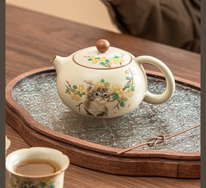 Detailed view of handmade ceramic teapot with cat motif and wooden lid on tea tray