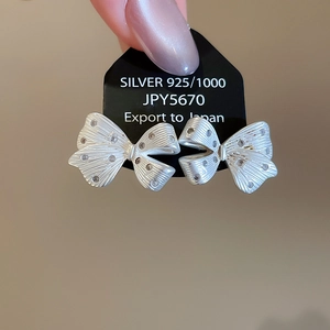 Detailed macro view of 925 silver bow earrings with brushed texture and zircon accents