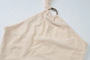 Close-up of beige halter dress featuring soft fabric texture and metallic ring detail