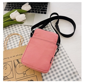 Close-up of pink corduroy mini crossbody bag with black nylon strap on aesthetic desk