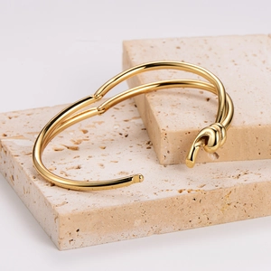 Detailed close-up of a high-polish gold knot cuff bracelet on natural stone texture
