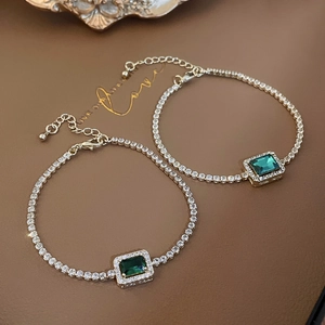 Detailed close-up of emerald green geometric stone tennis bracelet with gold finish