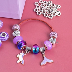 Detail of DIY charm bracelet with unicorn and mermaid tail pendants on pink background