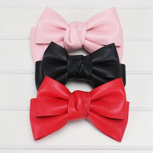 Detailed view of PU leather bow hair clips in pink, black and red on white wood