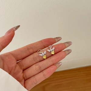 Macro shot of bee-shaped earrings with yellow heart stones and zircon wings on hand