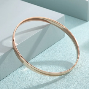 Polished rose gold stainless steel bangle resting on a blue geometric display stand