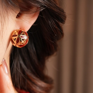 Gros plan de boucles d'oreilles vintage fleurs ajourées dorées et émail rouge sur modèle