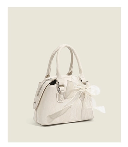 Détail d'un sac Boston crème avec un grand nœud en dentelle et finitions argentées