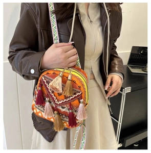 Detailed view of an orange bohemian round crossbody bag with tassels and woven patterns