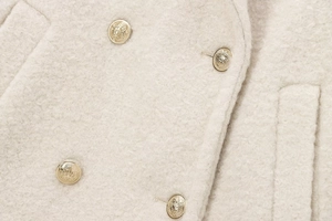 Close-up of premium white bouclé coat fabric with four decorative gold crest buttons