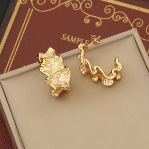 Detailed close-up of golden irregular wavy stud earrings with polished metallic texture