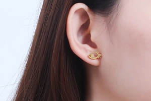 Close-up of a gold eye-shaped stud earring with eyelash detail worn by a model