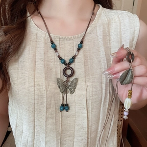 Detail of vintage necklace with butterfly charm, wooden rings and blue beads on a beige shirt