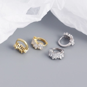 Close-up of gold and silver hoop earrings with rectangular zircon stones on white paper