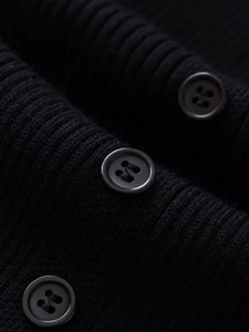 Detailed close-up of black ribbed knit fabric and matching four-hole buttons on a midi dress