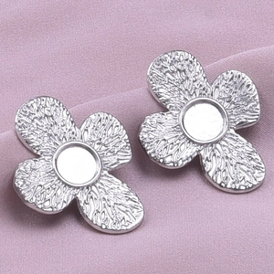 Detail of silver flower stud earrings with textured petals on a lilac fabric background