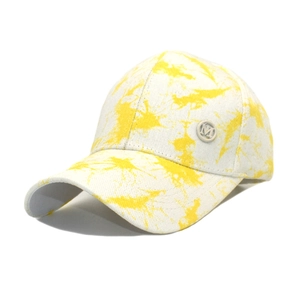 Detail of yellow tie-dye cotton baseball cap with metallic M letter logo and curved brim