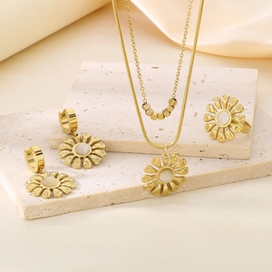 Detailed set of gold flower jewelry with pearls on beige stone and silk backdrop