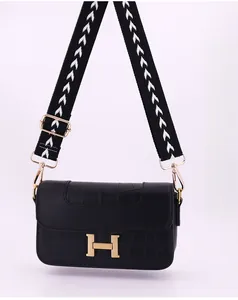 Detail of black crocodile texture bag with golden H buckle and geometric fabric strap