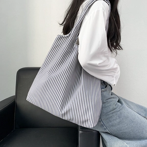 Minimalist blue and white striped canvas tote bag shown on model in a modern studio setting