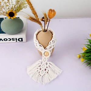 Bohemian hand-woven cotton curtain tieback with a wooden bead and tassel on a ceramic jar