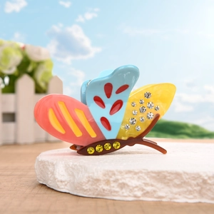 Colorful butterfly hair claw clip with rhinestones on a decorative stone base