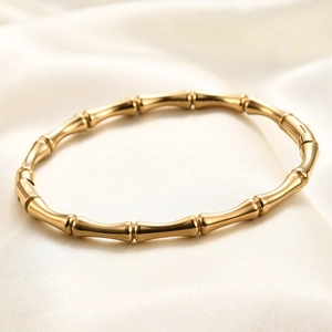 Close-up of golden bamboo-shaped stainless steel bangle on soft white silk background