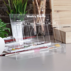 Detailed view of acrylic weekly planner board with metal stands on a desktop setup
