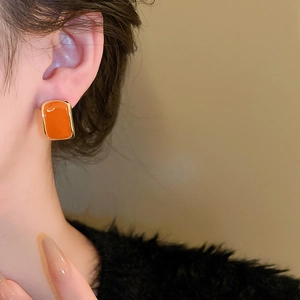 Close-up of vintage orange enamel square stud earring with gold border on model