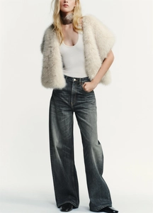 Detail of grey wide-leg jeans paired with cream faux fur vest and white tank top