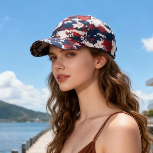 Digital red and blue camo baseball cap worn by model in a sunny outdoor lakeside setting