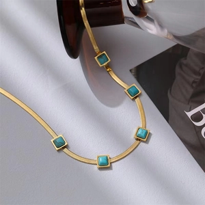 Collana a catena piatta a serpente dorata con pietre turchesi quadrate su sfondo bianco