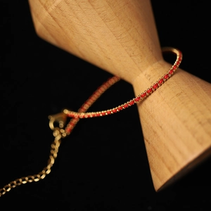 Detail of red and gold beaded cord bracelet with lobster clasp on a wooden display
