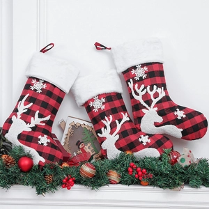 Three red and black plaid Christmas stockings with embroidered reindeer on a festive mantel