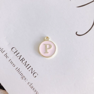 Close-up of golden round pendant with pink enamel and a gold letter P charm