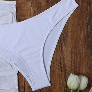 Bikini tre pezzi bianco con slip a vita alta e top in rete su fondo in legno