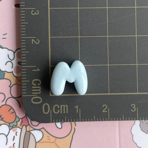 Detailed view of a light blue resin letter M charm on a scale showing 1.5cm width