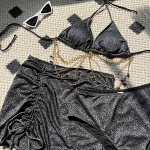 Flat lay of black glitter bikini set with gold chain detail and drawstring skirt