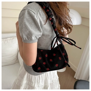 Detail of black corduroy underarm bag with red strawberry print and bow shoulder strap