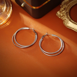 Double-layer silver hoop earrings featuring polished and frosted textures on orange leather