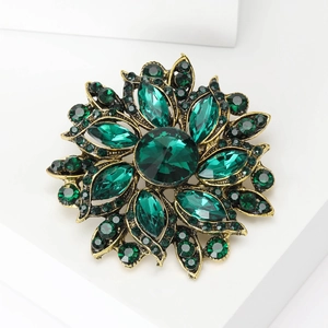Detailed close-up of a vintage flower brooch with deep green crystals and antique gold finish