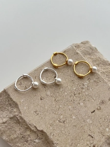 Detail of silver and gold pearl hoop earrings displayed on a natural beige stone