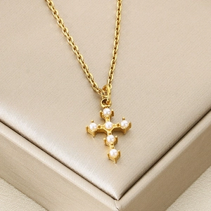 Detail of cross pendant with inlaid pearls on gold chain over champagne satin