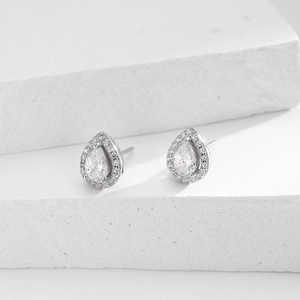 Macro shot of silver teardrop stud earrings with pear-cut main stone on white stone background