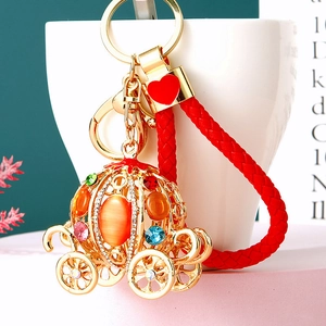 Macro detail of golden pumpkin carriage keychain with colorful rhinestones and red woven strap