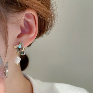 Macro side view of a butterfly pearl earring with shell inlay and zircons on a model